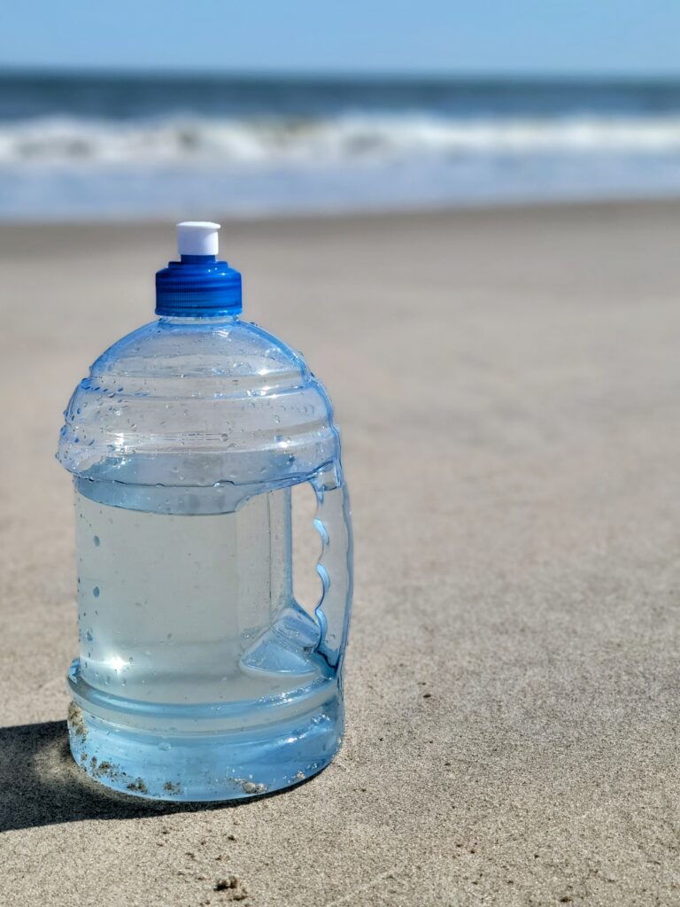 A water bottle sitting on the beach next to the ocean.