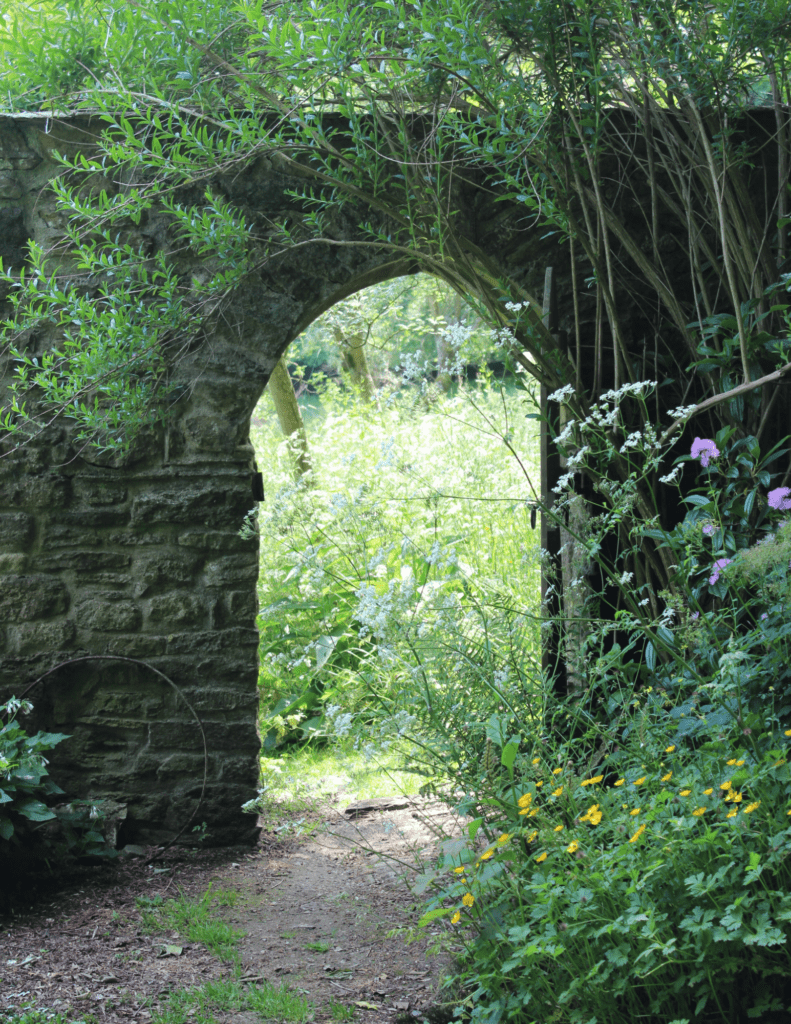 A stone arch in the middle of a garden.